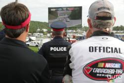 Police and NASCAR official watching the end of the race on the big screen in pit row