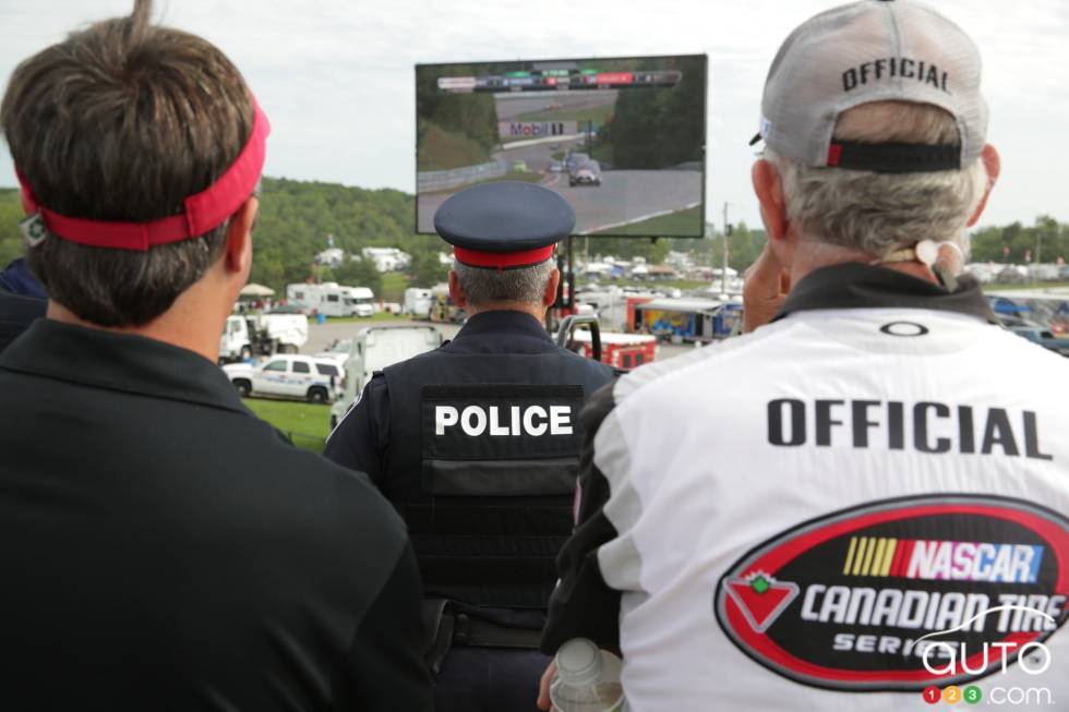Police and NASCAR official watching the end of the race on the big screen in pit row